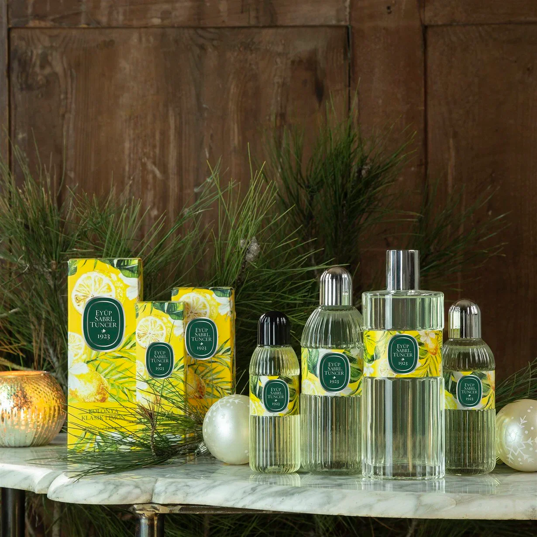 Eyüp Sabri Tuncer Klasik Limon kolonya collection — bottles and gift boxes arranged on marble with pine branches and golden candlelight